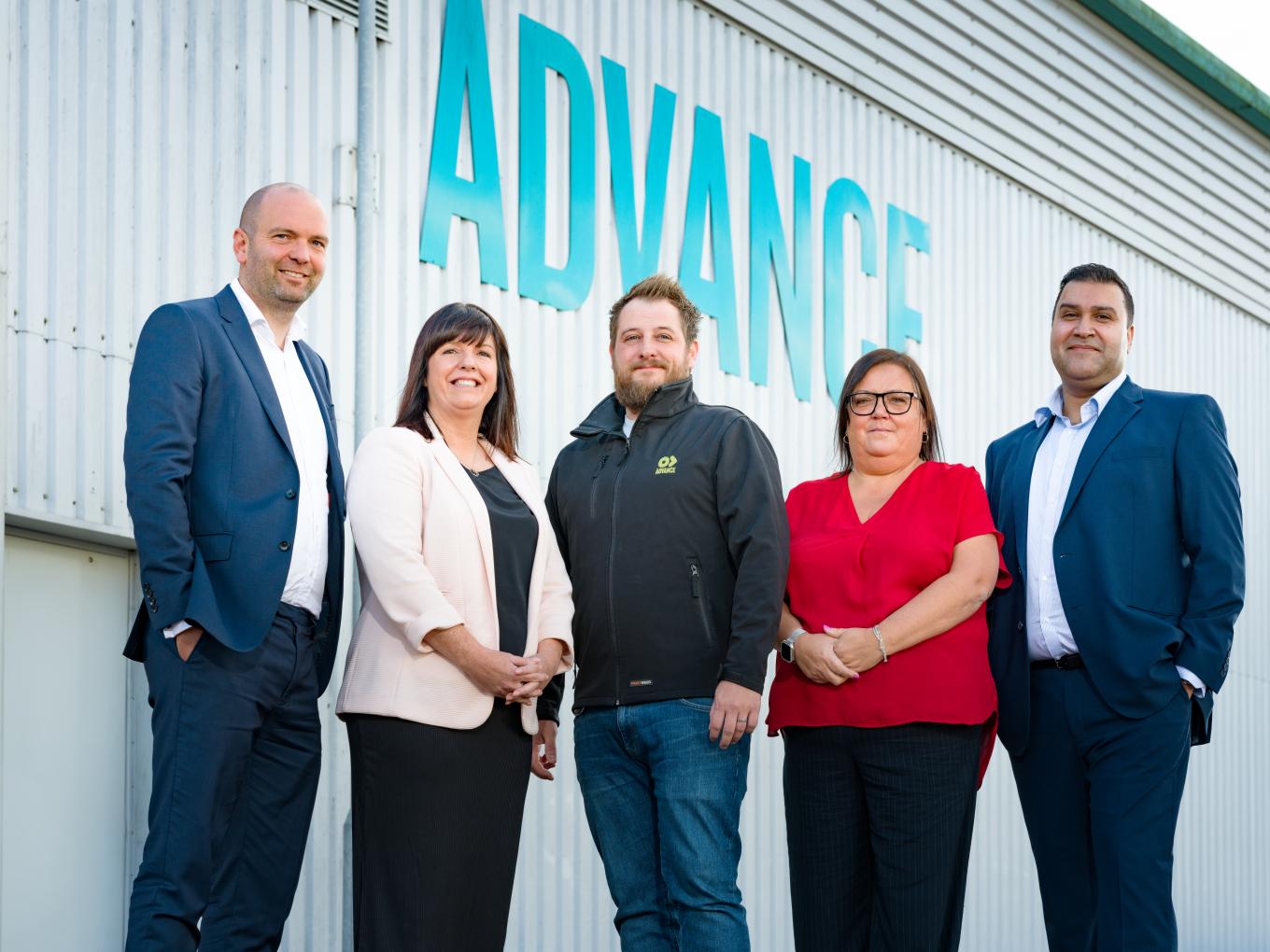 Group of 5 people standing in front of Advance branding signpost